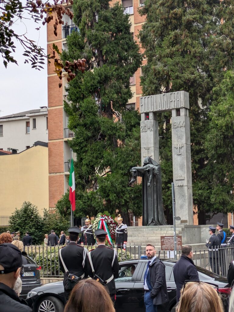 Foto del monumento ai piccoli martiri di gorla. Due colonne in pietra recano la scritta "Ecco la guerra" e la data della strage, 20 ottobre 1944. Davanti alle colonne una statua bronzea raffigura un uomo che solleva il corpo senza vita di un bambino